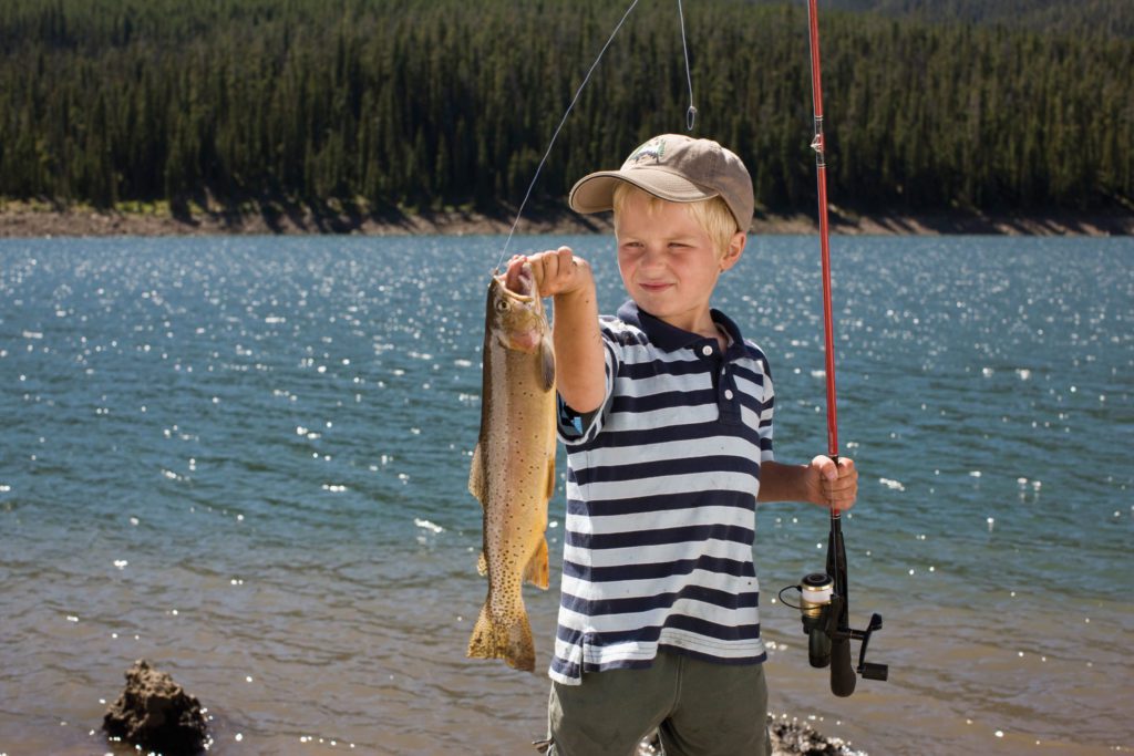 A little boy with a fishing rod and a large fish he caught.