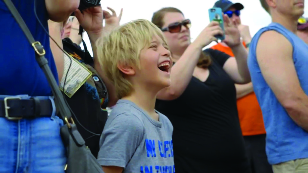 A little boy laughs as a crowd takes pictures with their phones.