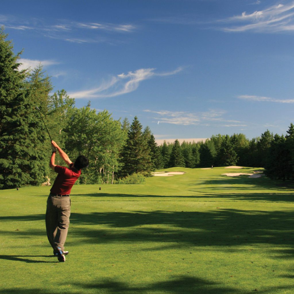 A man swings his golf club on the green.