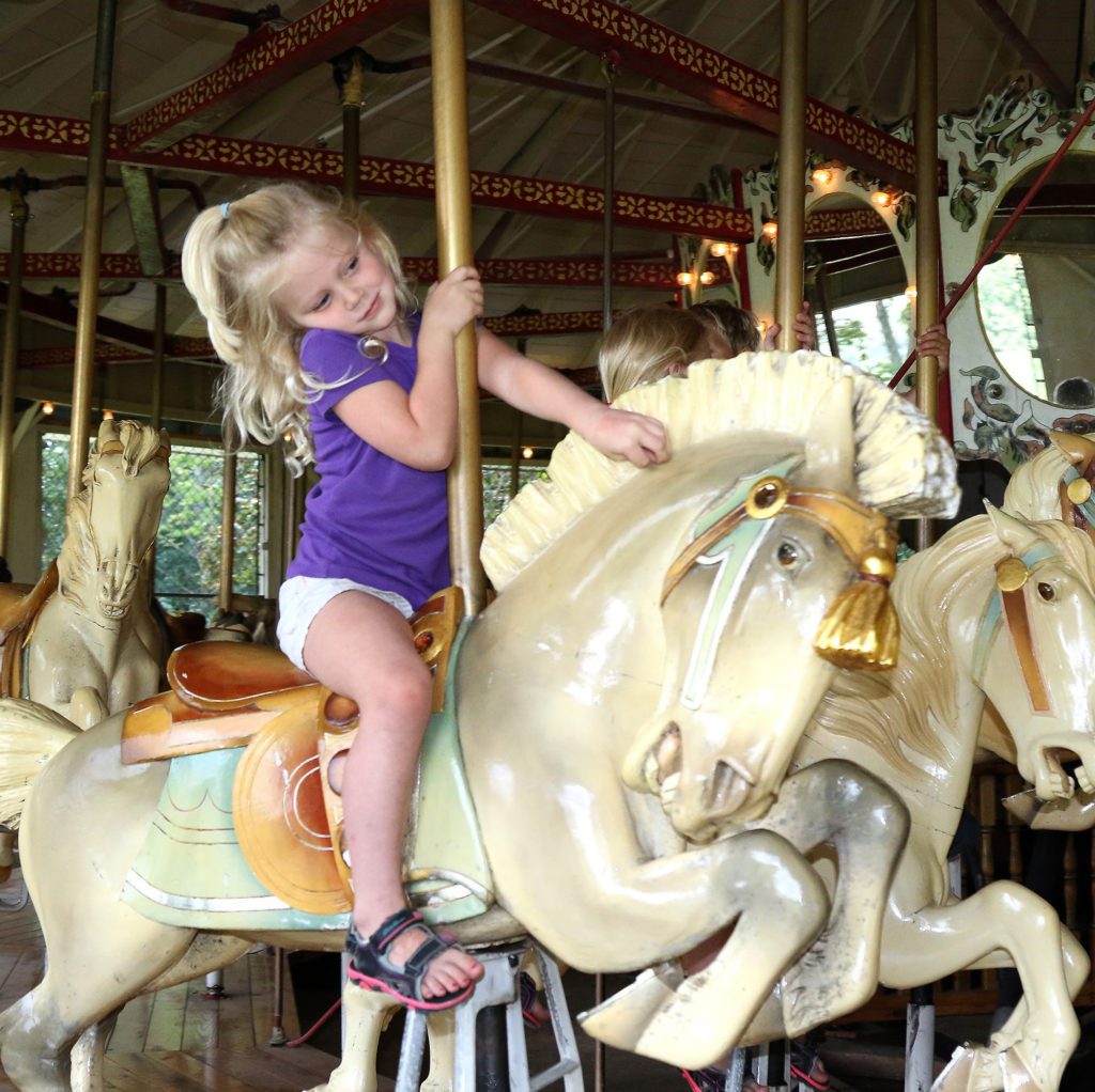 A little girl riding a white carousel horse.